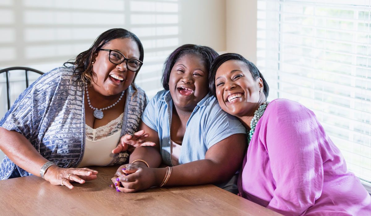 Three women laughing together at a kitchen table at home