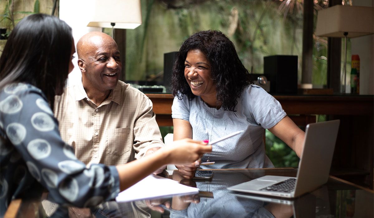 Three people talking together at a table with a laptop